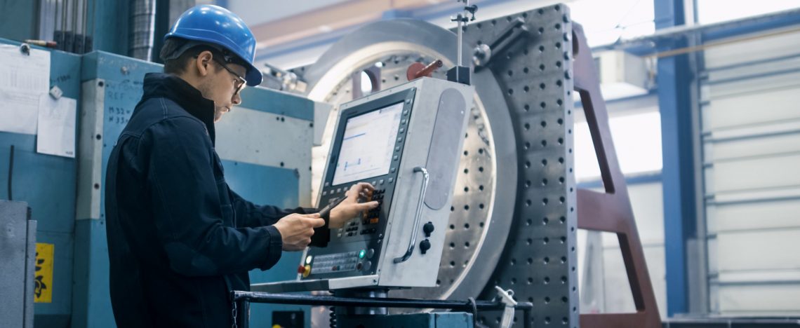 Factory worker is programming a CNC milling machine with a tablet computer.